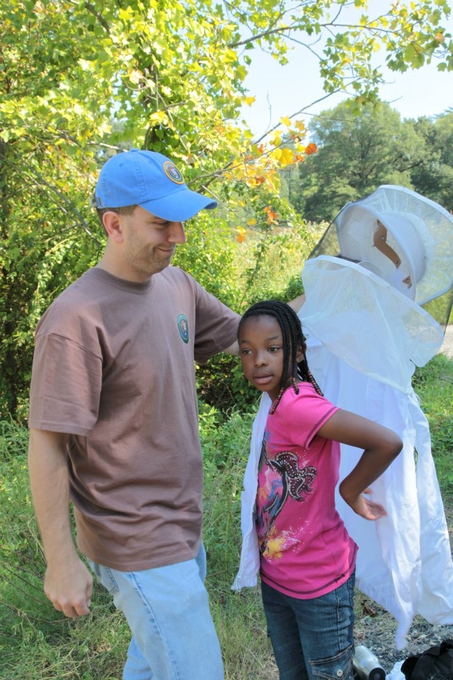 Volunteer David helps a future bee keeper with her jacket and vail