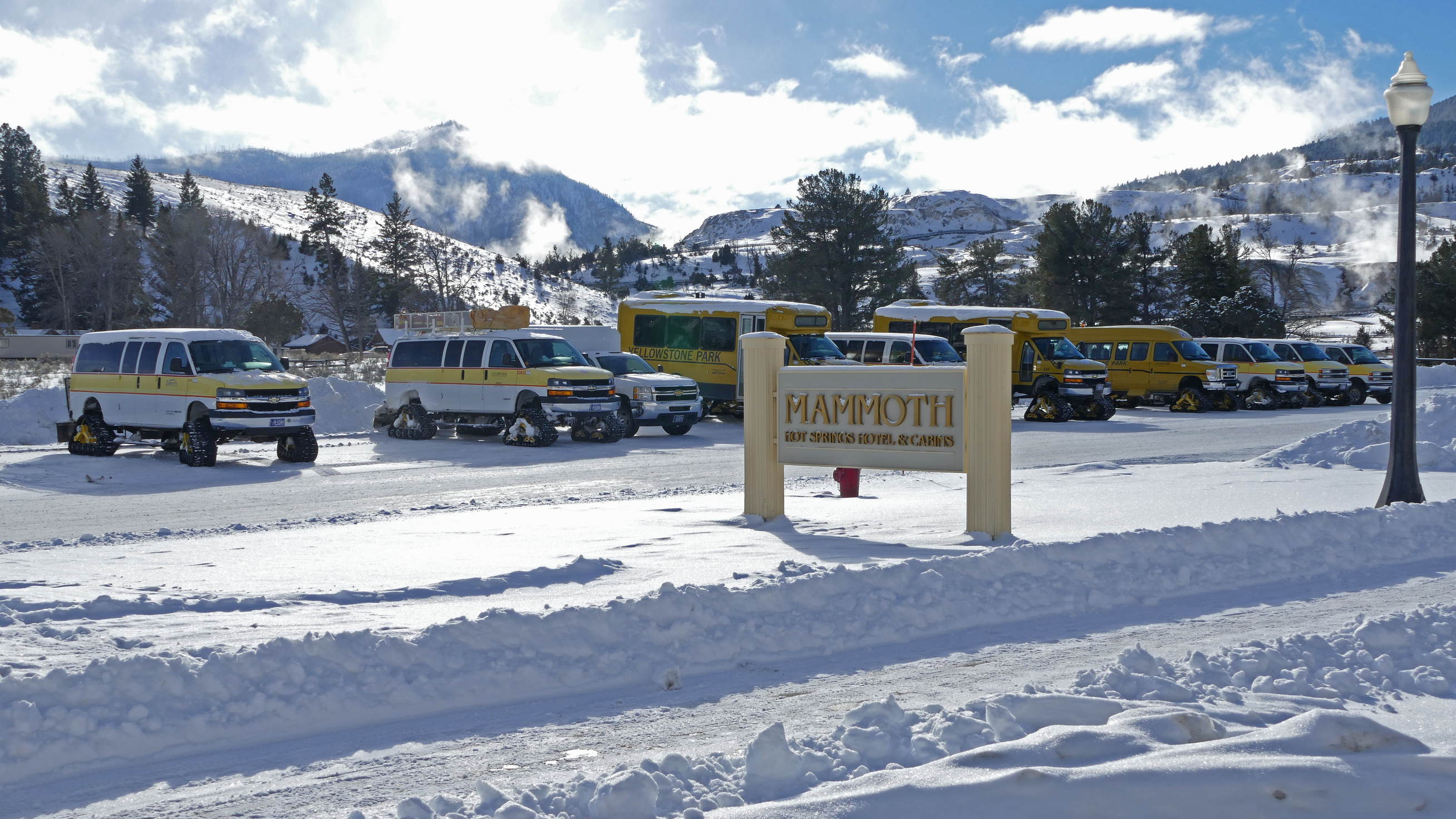 Vans with tracks instead of wheels sit in a line behind the sign for Mammoth Hot Spring Hotel