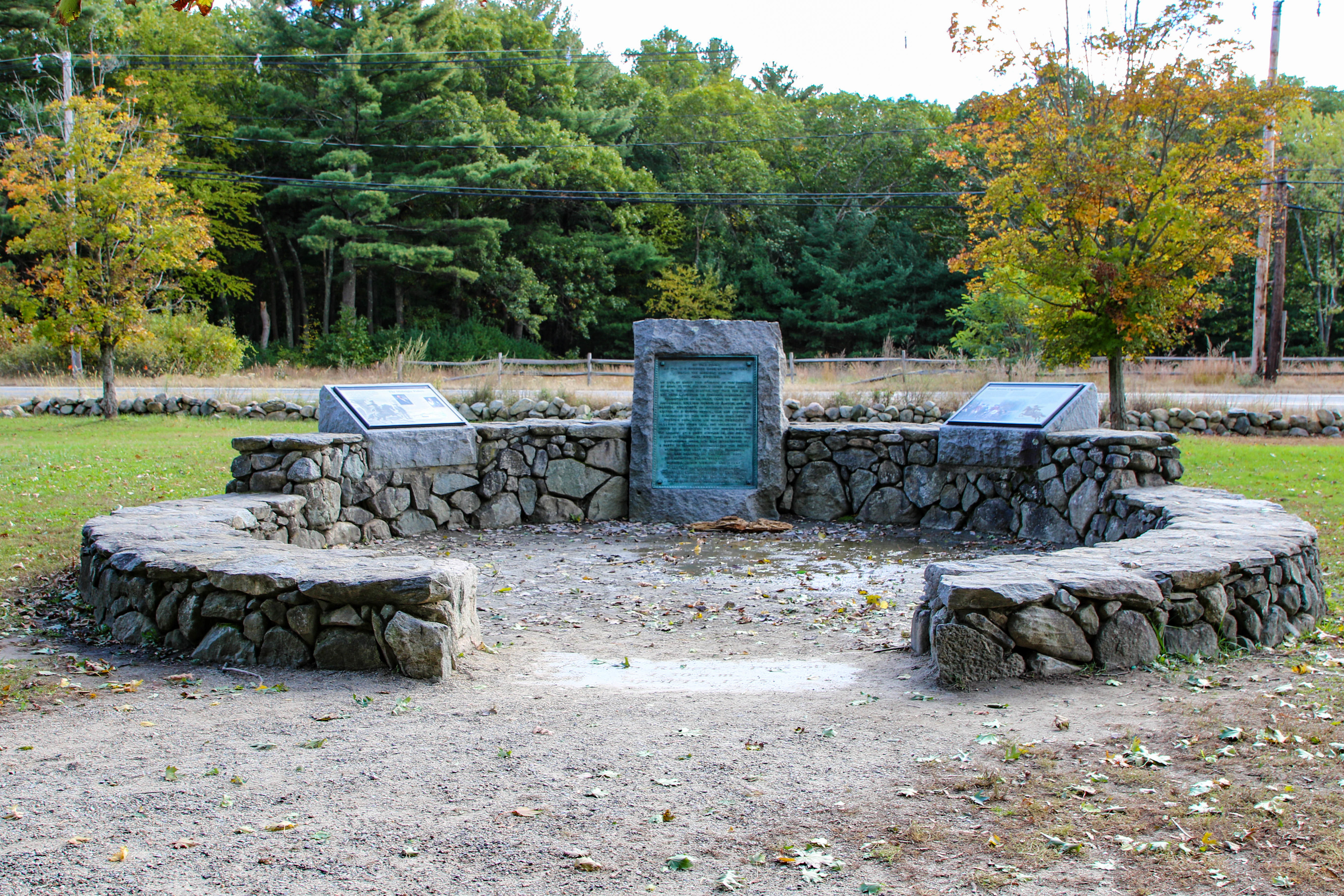Circular stone memorial with a plaque and interpretive signs