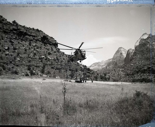 Pilot module from F-111 aircraft which crashed behind Zion Lodge July 11, 1973. Helicopter and truck from Nellis Air Force Base loading module near field in front of Visitor Center.