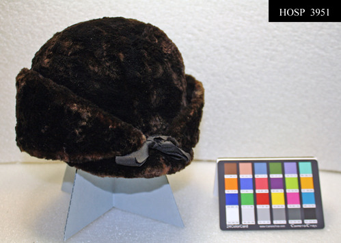 Man's sealskin cap with ear flaps.  Ribbon ties at front of earflap section; brown quilted satin lining around edge, smooth satin lining inside crown, Dark brown manufacturer's label embroidered with gold thread, sewn to lining.