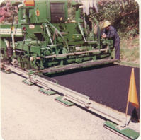 Barber-Greene laydown machine placing bituminous binder. Automatic screed control device in foreground