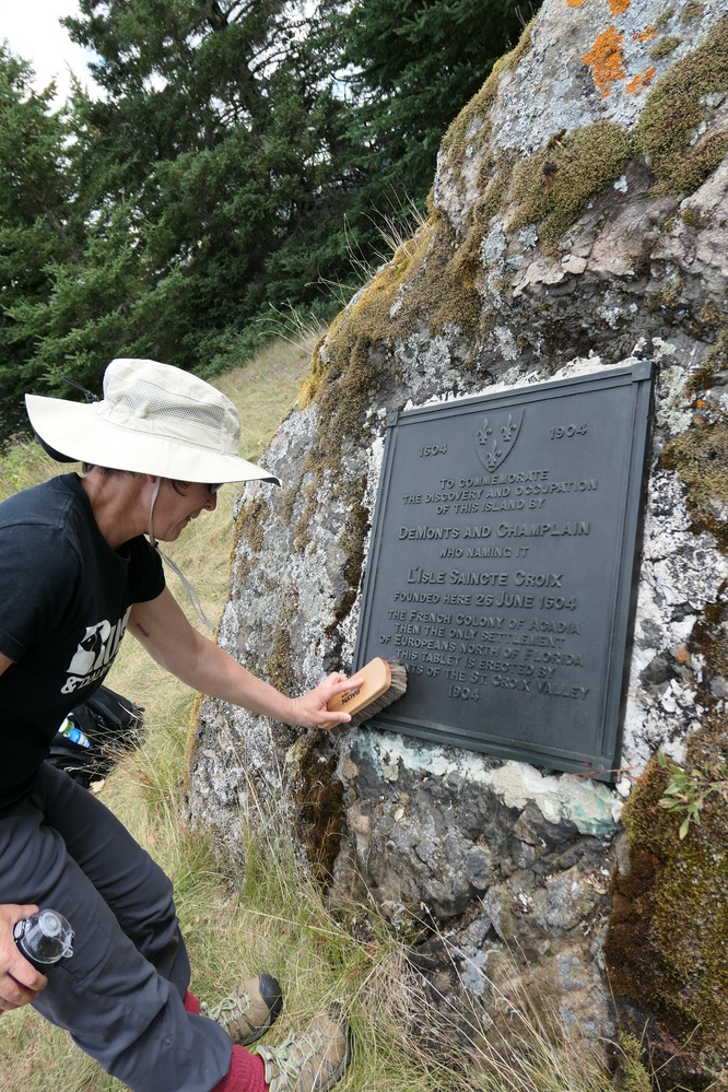 A woman lightly buffs the cold surface of a bronze plaque, using a shoeshine brush.
