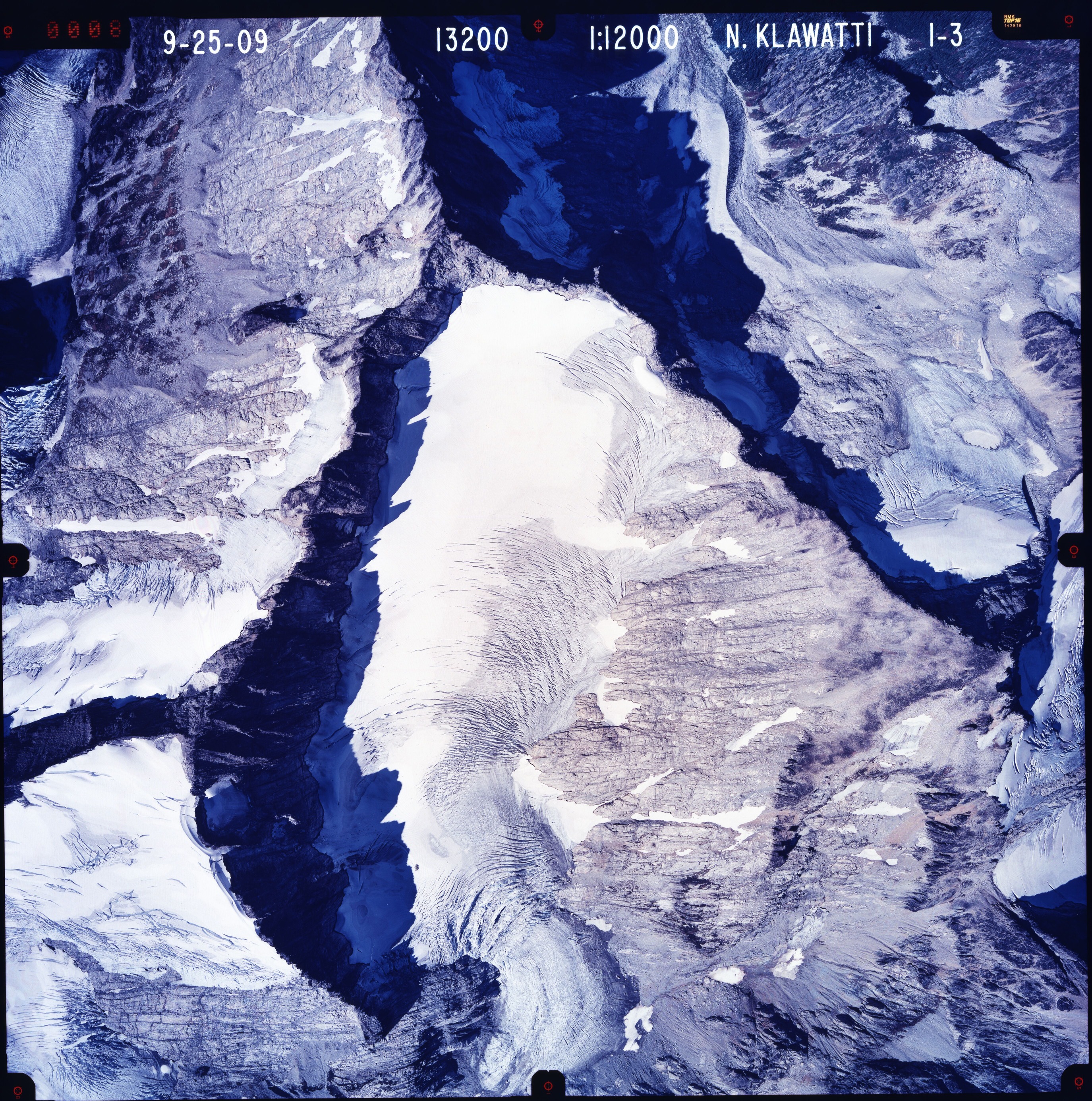 Color aerial photograph of glacier, snowfields and alpine lake on mountain peak.