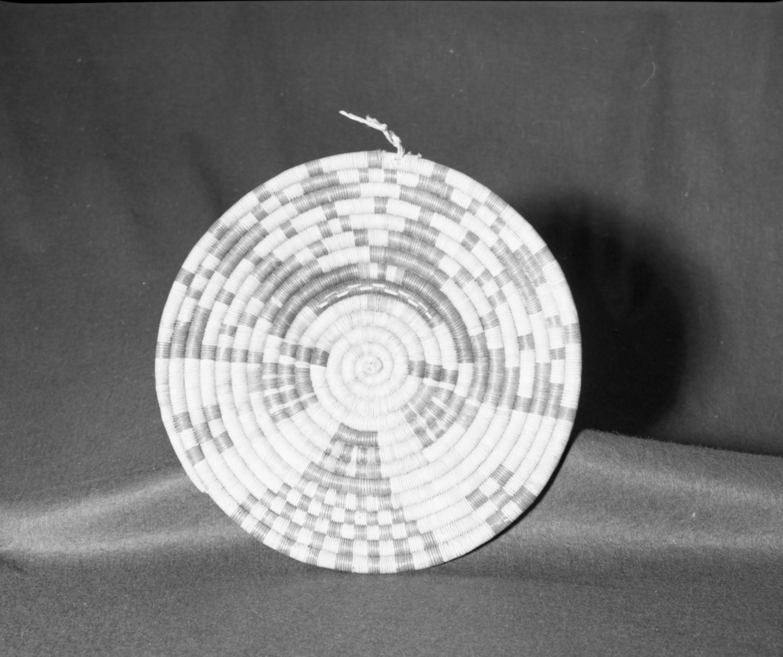 Marie Rozier Collection, Catalog No. 5. Object: Hopi coiled plaque. Dimensions: 13 1/2''. Materials: Yucca, rabbit brush, dyes. Technology: Leftward coil direction, interlocking stitch, kachina face pattern. Collection History: From Second Mesa. Acquired by G. DuGay. Photographed by Michael Dixon in December 1982. Catalogued by Craig Bates and Barbara Beroza. Yosemite Collections, National Park Service.