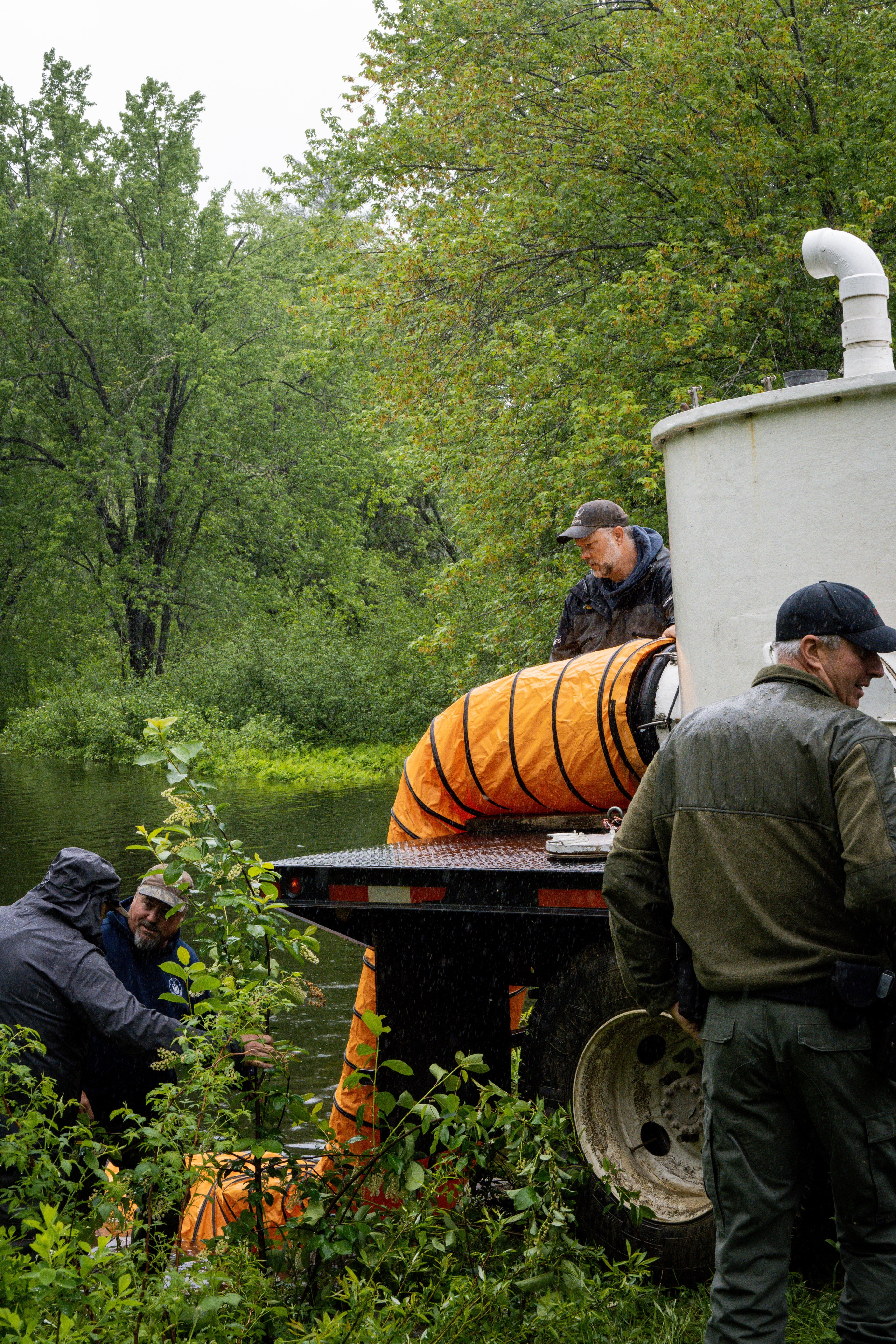 An orange tube connected to a water tank full of fish has been placed in the river.