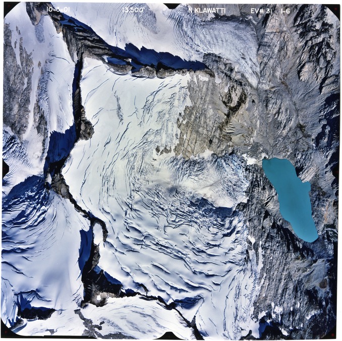 Color aerial photograph of glacier, snowfields, and alpine lake on mountain peak.