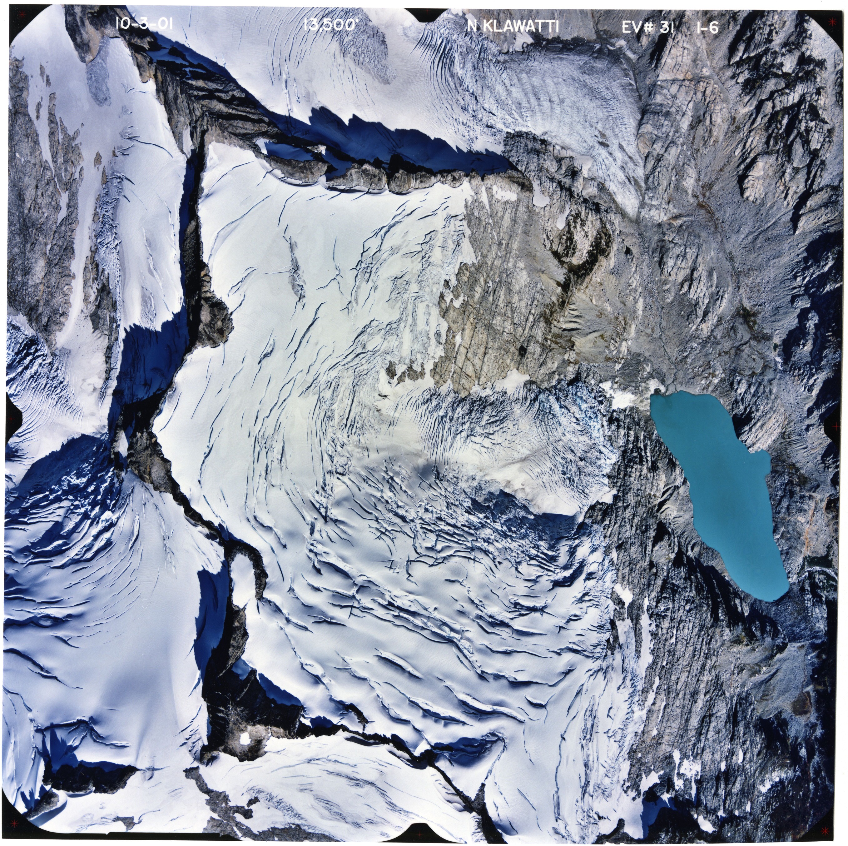 Color aerial photograph of glacier, snowfields, and alpine lake on mountain peak.