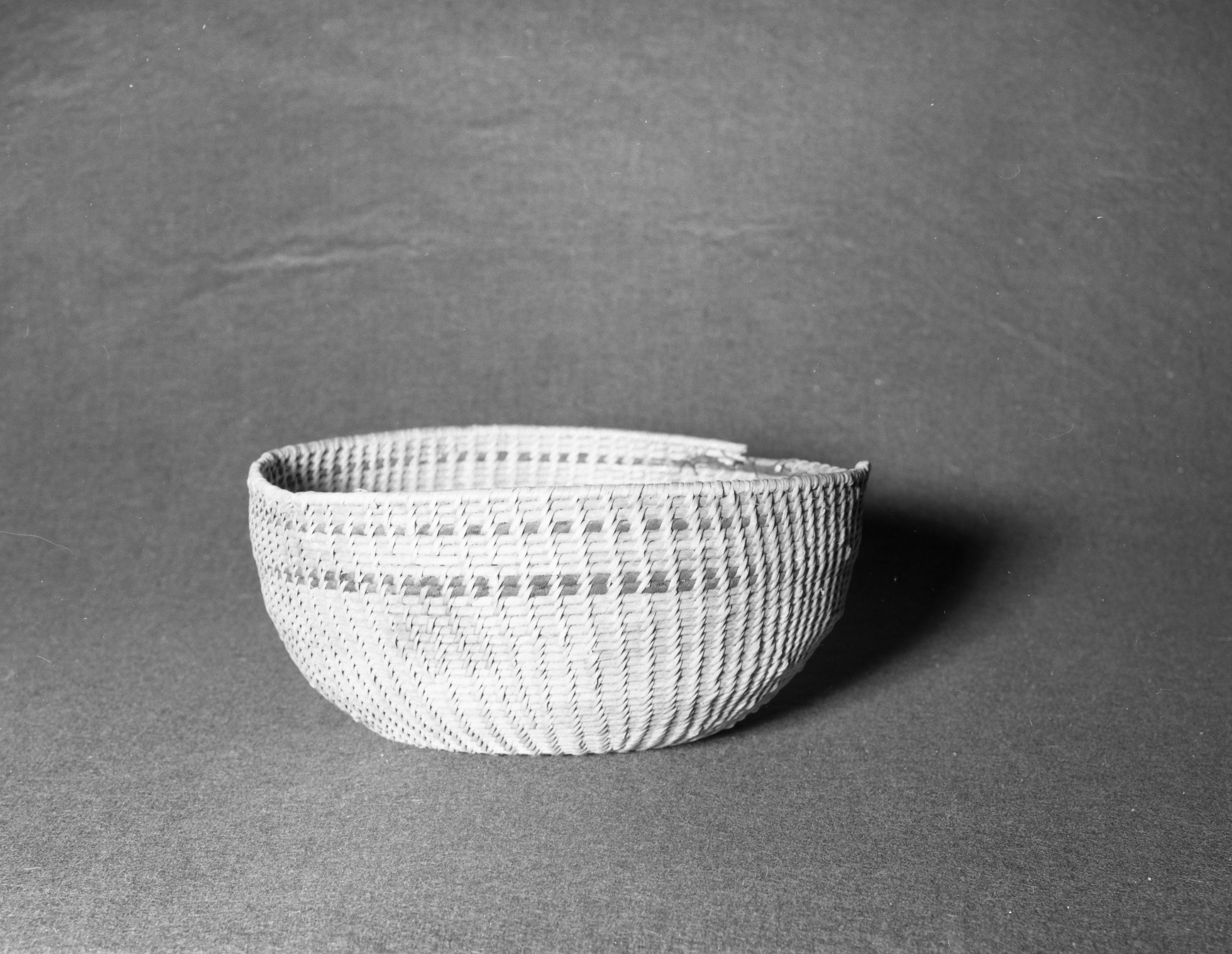 Mrs. Geraldine McConnel Collection. Object: Miwok basket. Dimensions: 9 1/2" x 4 1/4". Materials: Willow, black cotton cloth. Technology: Clockspring start, non-interlocking stitch. Collection History: Acquired from a Portuguese family that lived in Sonora and probably dates from before 1900. It is nearly identical to a basket in the collection of the State of California, Dept. of Parks & Recreation, that was acquired in Columia c. 1867. Photographed by Michael Dixon in January 1983. Catalogued by Craig Bates and Barbara Beroza. Yosemite Collections, National Park Service.