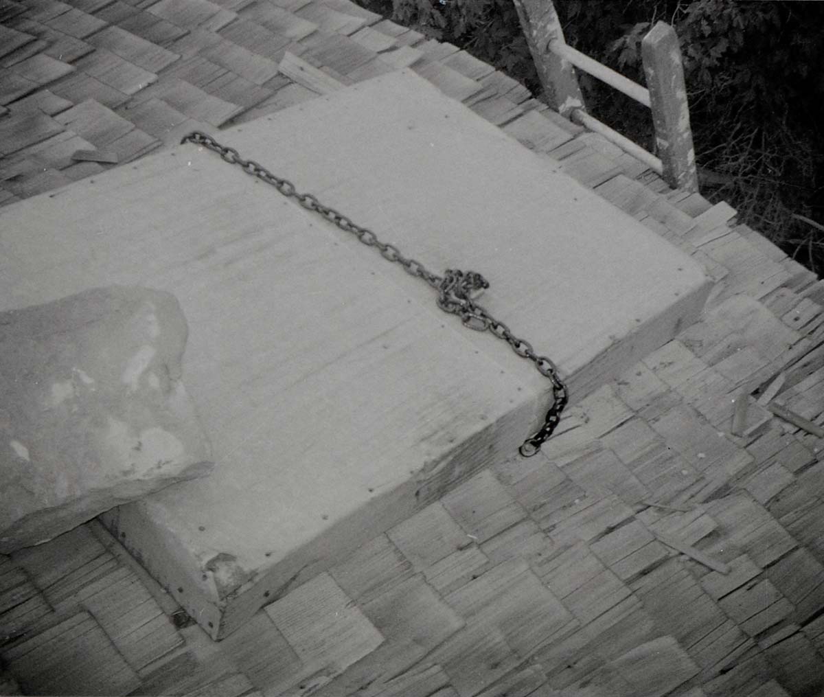 Large rock, chain, and lock on hatch of water tank roof, prior to reroofing project.