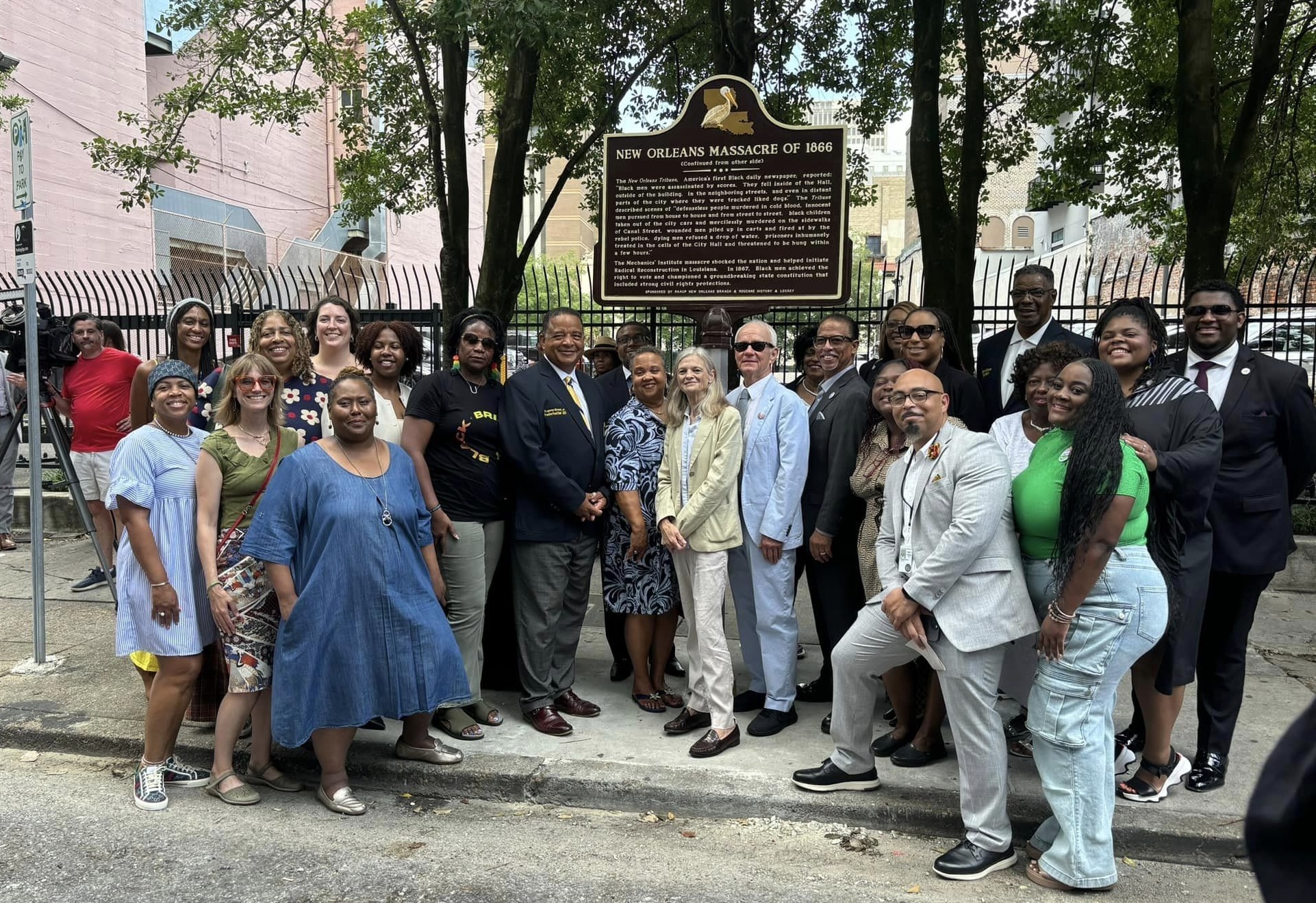 A large group of people stand in front of a new sign about the New Orleans Massacre of 1866.