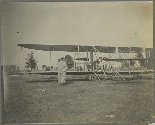 An early airplane on a field with people standing next to it.