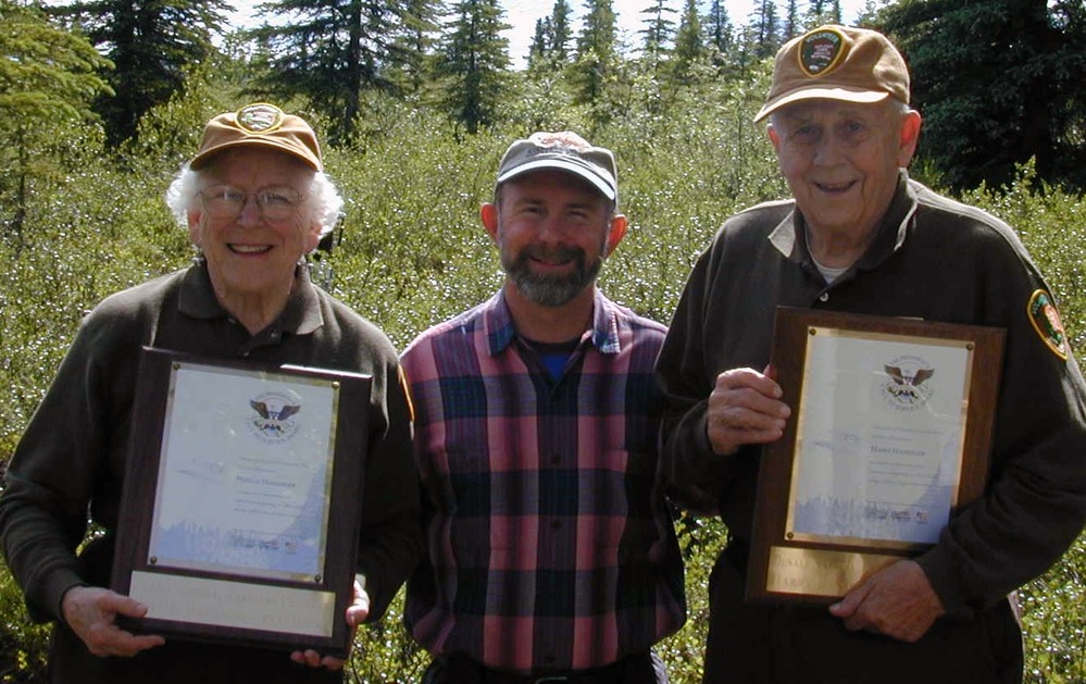 three people smiling, two holding plaques