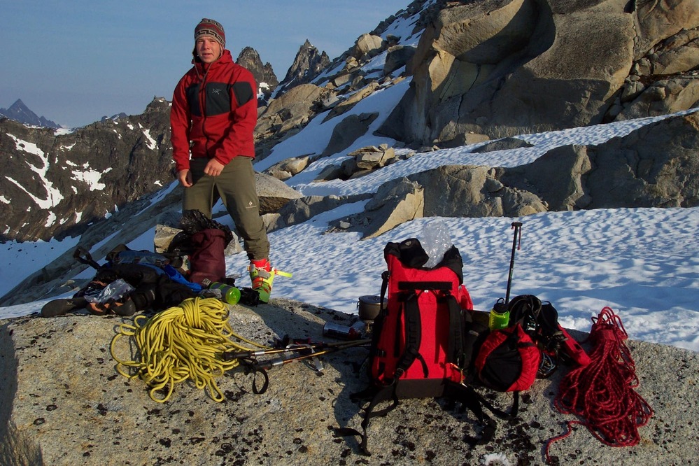 man standing on a rock near a glacier, in front of steep mountains