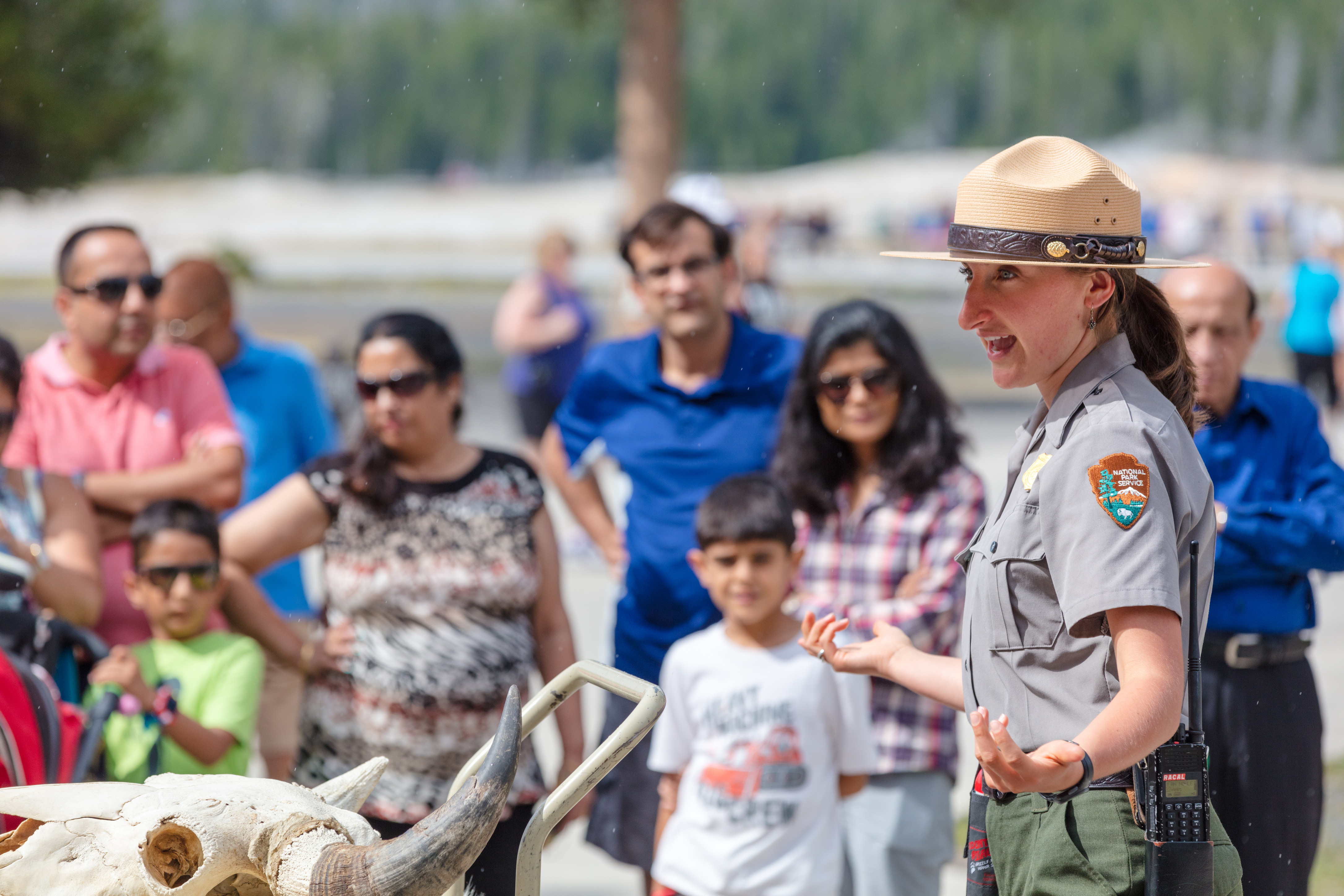 A female ranger talks to a group of people and has a cart with animal skulls on it.