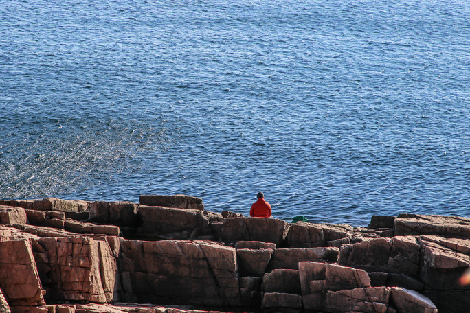 Visitor sitting on rocky coastline next to the ocean