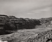 Black and white photograph of a grassy valley with steep rounded sides with buildings at the top