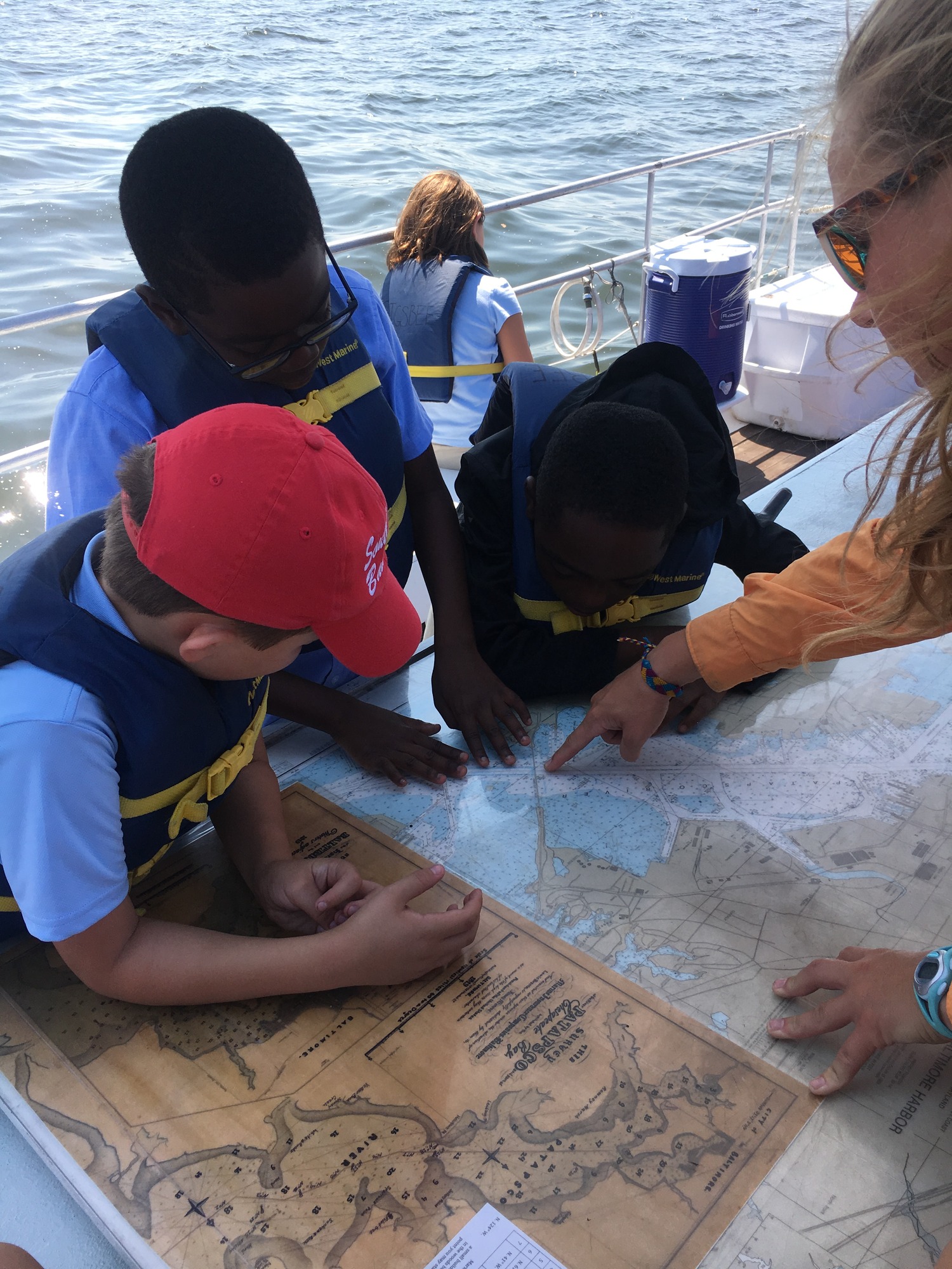 Three children look at a map provided by a woman.