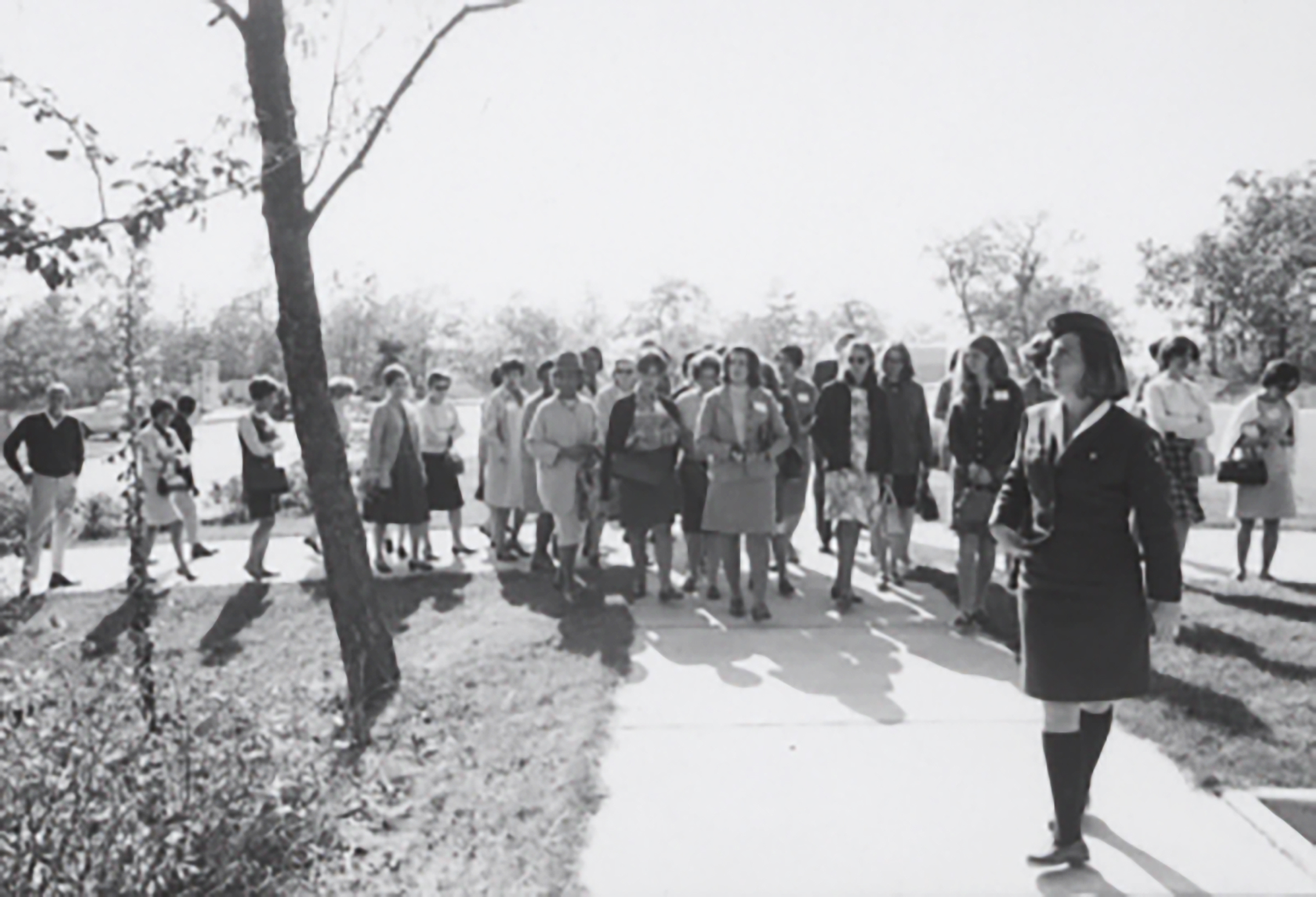 Woman in her NPS uniform stands in front of a tour group on a sidewalk. 