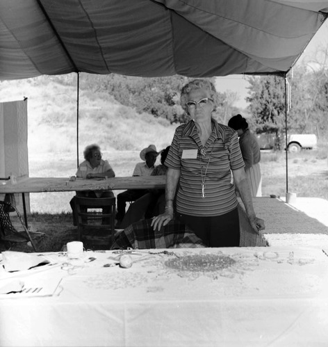 Woman standing with doily making demonstration table. Floyd DeMille in background with his family. Third annual Folklife Festival, September 7-8, 1979 at Zion National Park Nature Center.
