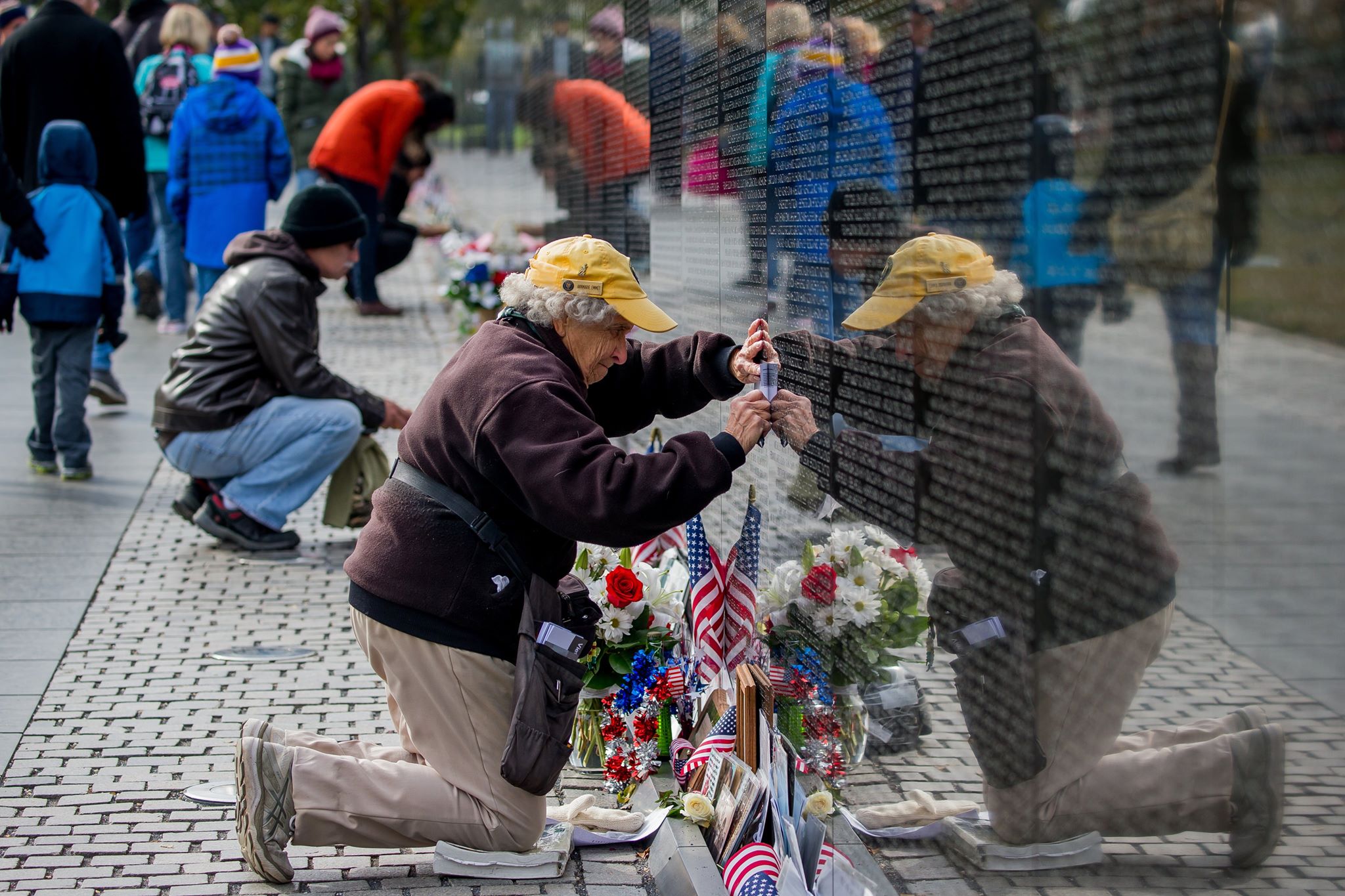 A National Park Service volunteer kneels and uses paper and a graphite stick to obtain a rubbing of a name from the Vietnam wall.