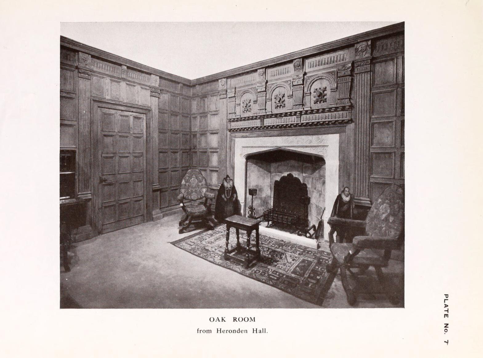 A black and white photograph of furniture around a fireplace and wooden panels.