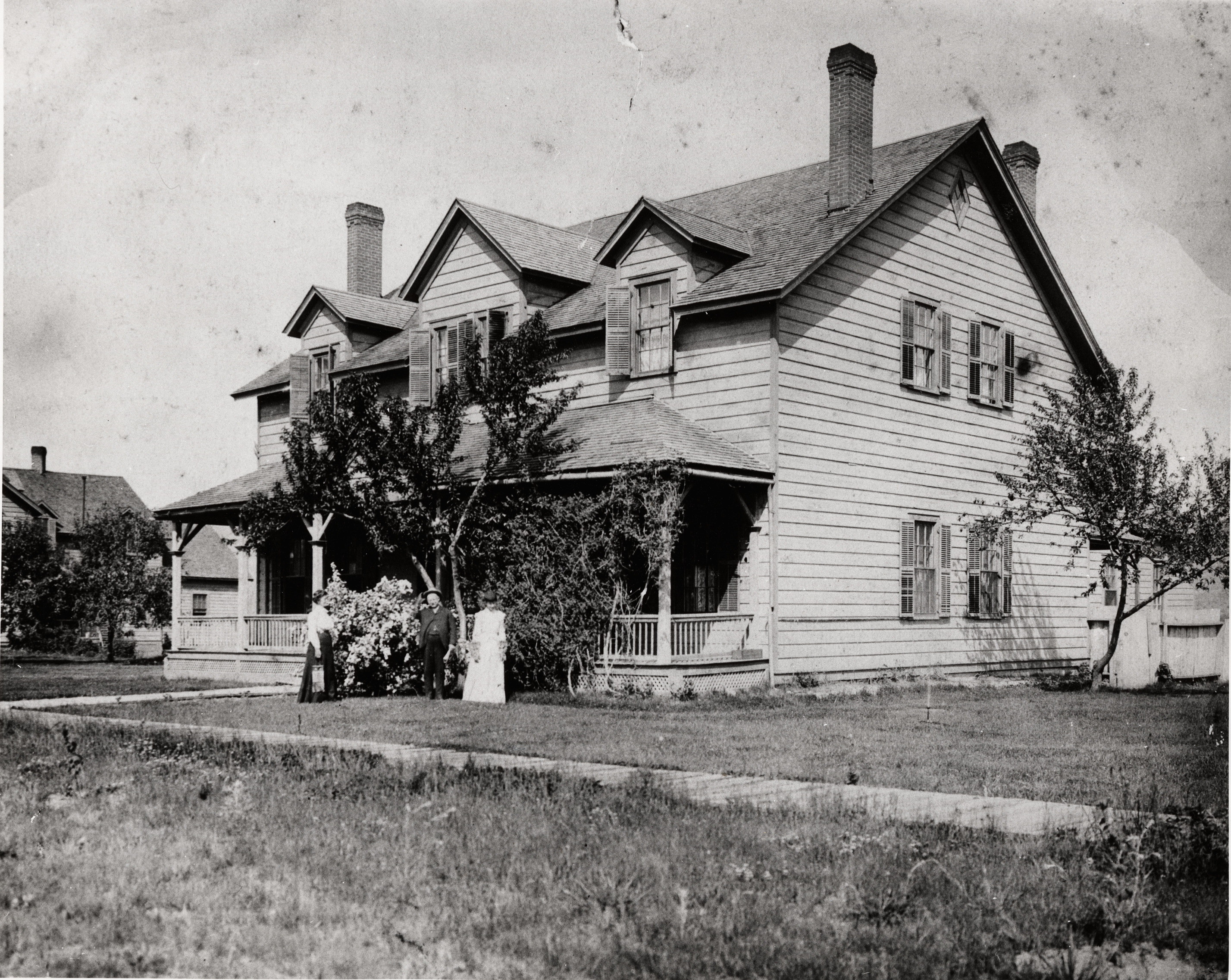 Black and white photograph of a two story house with three people in the yard