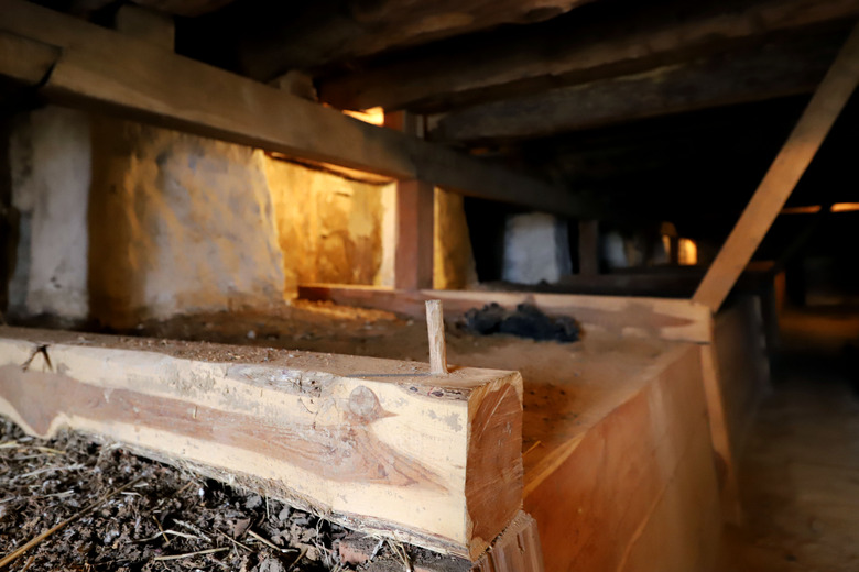 Basement with wood and dirt foundation in foreground and stone wall in background. 