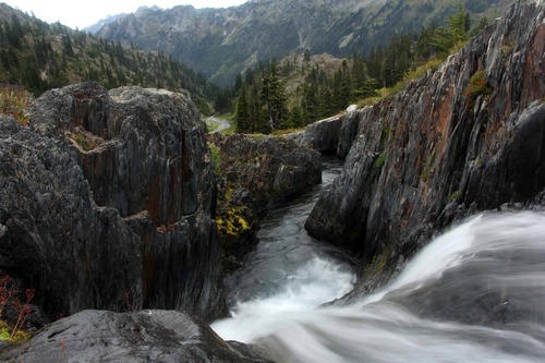 A river cascading between steep rock walls, viewed from the top of a waterfall.