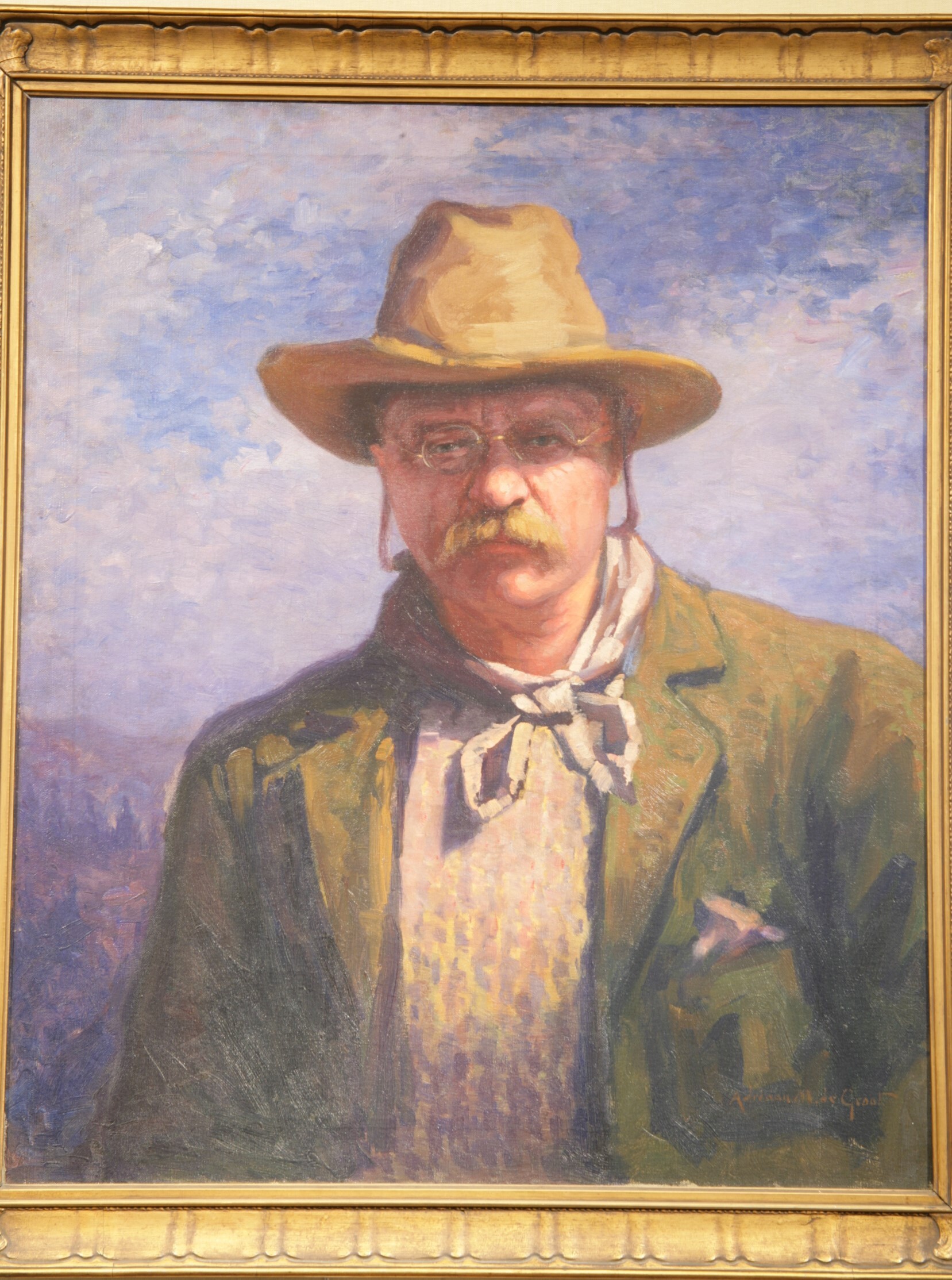 A portrait of Theodore Roosevelt's head and shoulders. He has a mustache and is wearing pince-nez glasses and a large brimmed hat. He has an open coat, a bandanna tied around his neck, and a handkerchief in his pocket. He looks intently at the viewer with a serious expression. The colors of the portrait are soft yellow, blue, and brown. The strokes are impressionistic in style.