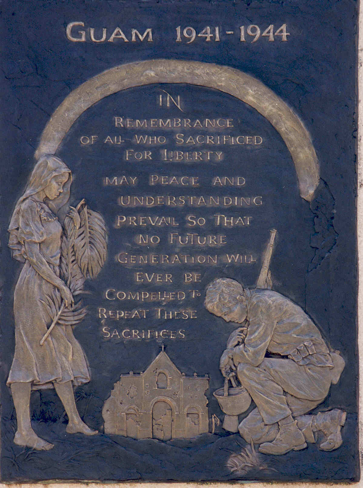 An engraved bronze plaque set into a concrete wall. It is labelled “Guam 1941-1944” and shows a man and a woman kneeling in front of a bombed-out church. The text says “In remembrance of all who sacrificed for liberty. May peace and understanding prevail so that no future generation will ever be compelled to repeat these sacrifices.”