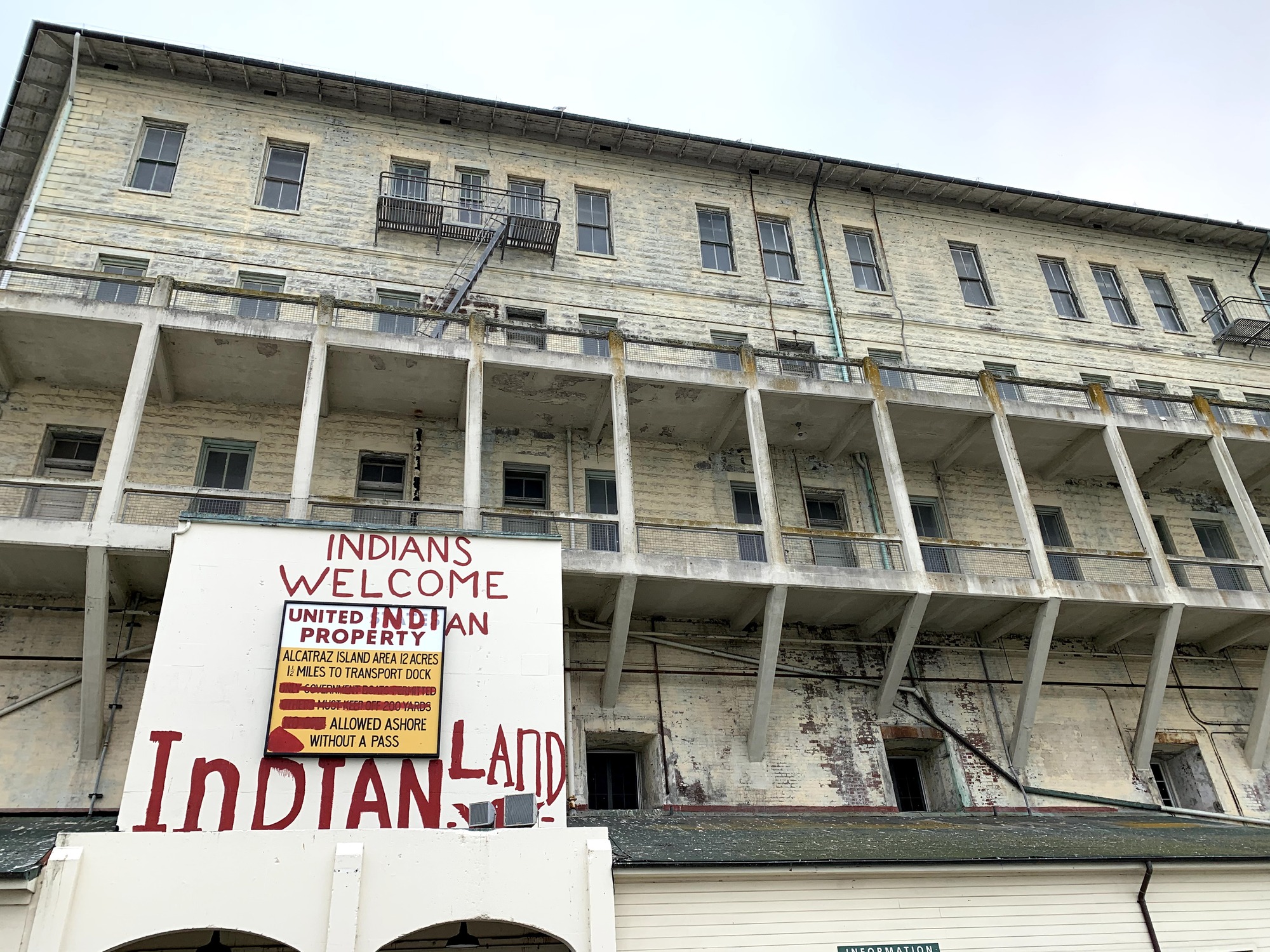 Political messaging painted on a white four-story concrete and brick apartment building reads "Indians Welcome - United Indian Property - Indian Land."