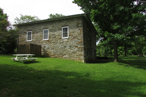 Picnic table and a tree beside a rectangular stone structure on a gently sloping grassy area