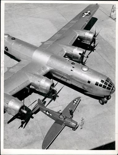 Black and white photo overhead shot of a grey airplane with four wing propellers and a white star on the wing. 