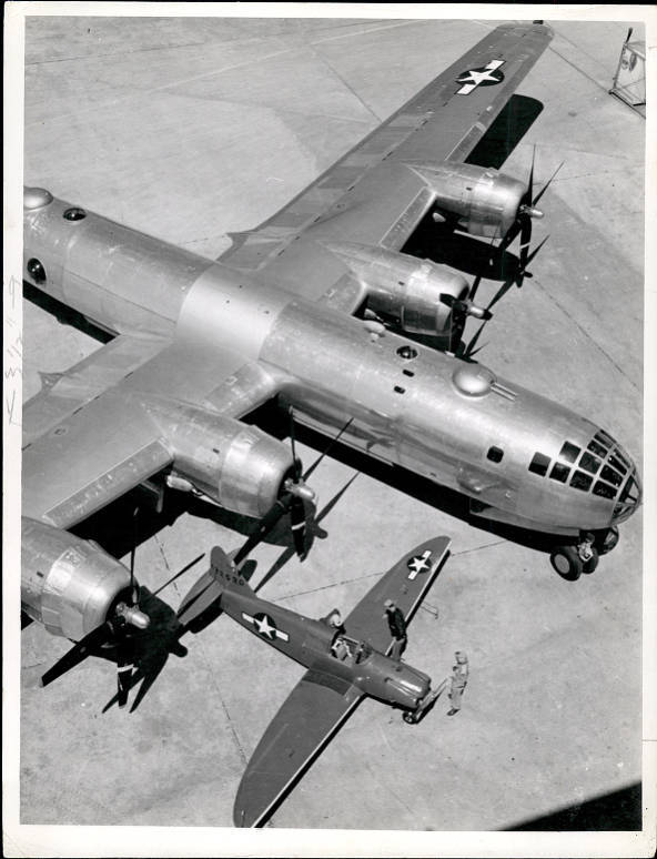 Black and white photo overhead shot of a grey airplane with four wing propellers and a white star on the wing. 