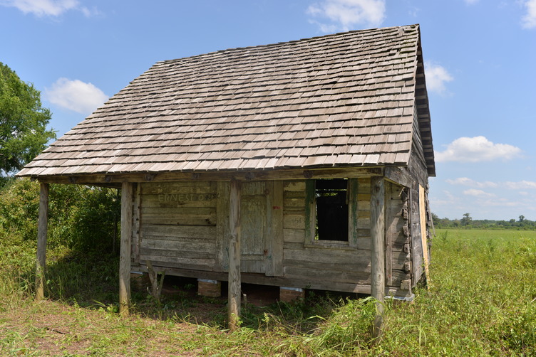Wooden cabin sits in a field.