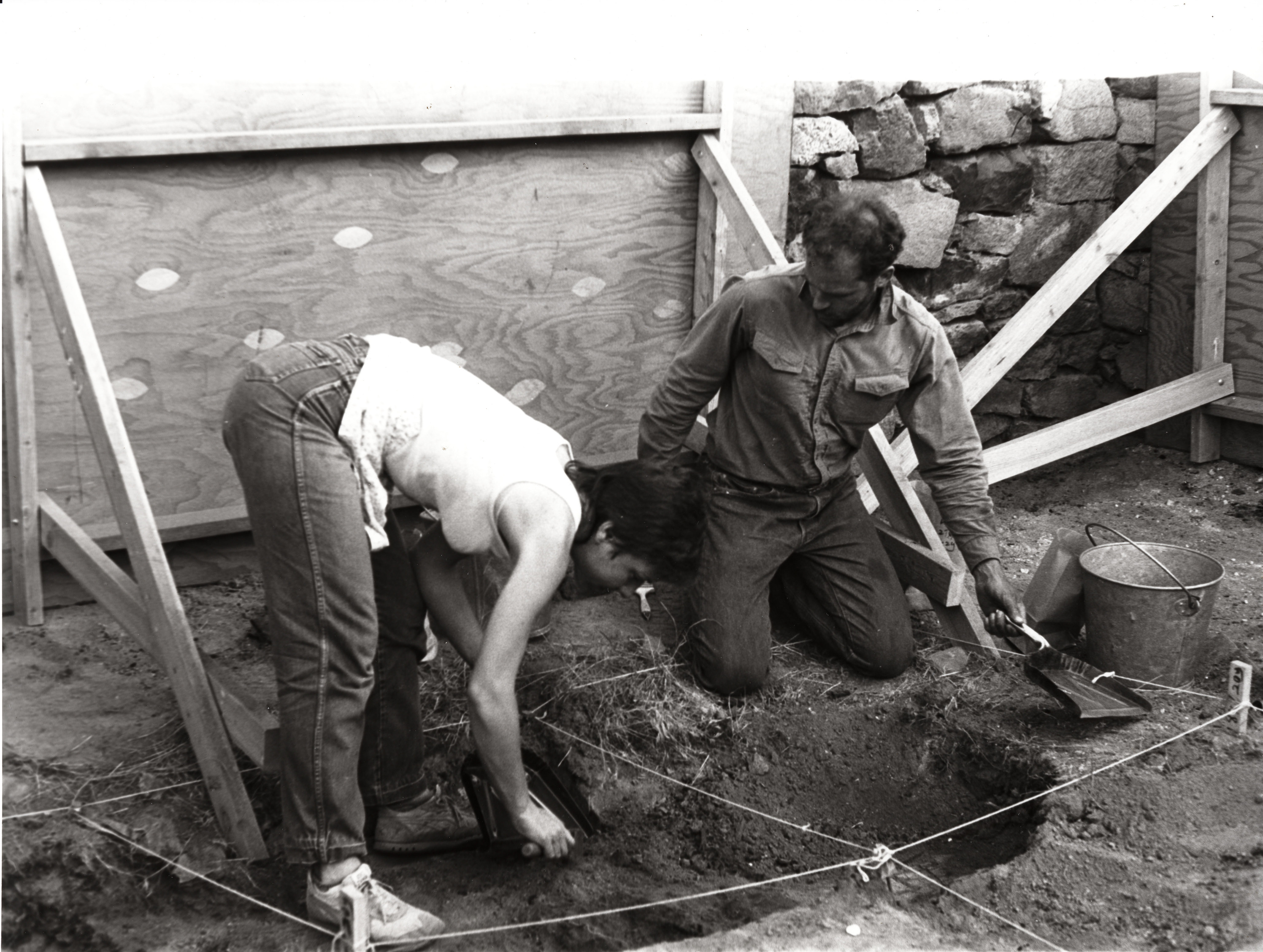 Black and white photograph of two people at an archeological dig. 