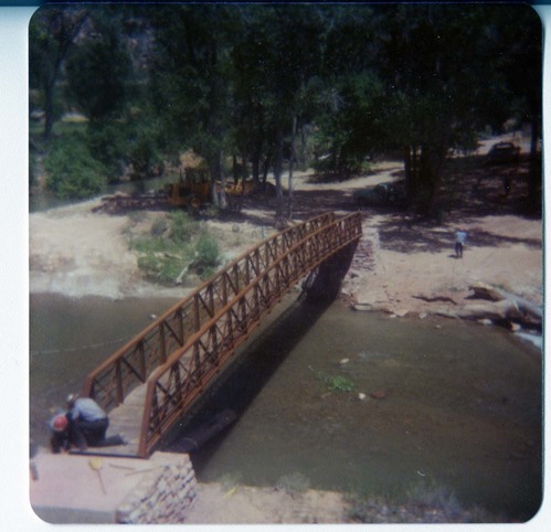 Two men working on the new Grotto footbridge across the Virgin River, equipment in background. Before trail created to access bridge.