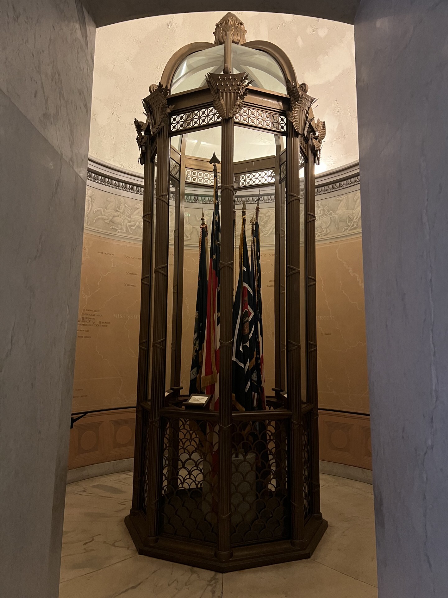 A small, circular room with a bronze display case with flags. There is a map on the back wall.