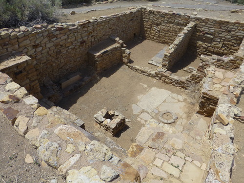 The rectangular ceremonial room inside Atsinna Pueblo showing a square wall recessed into the ground with several rock structures inside.