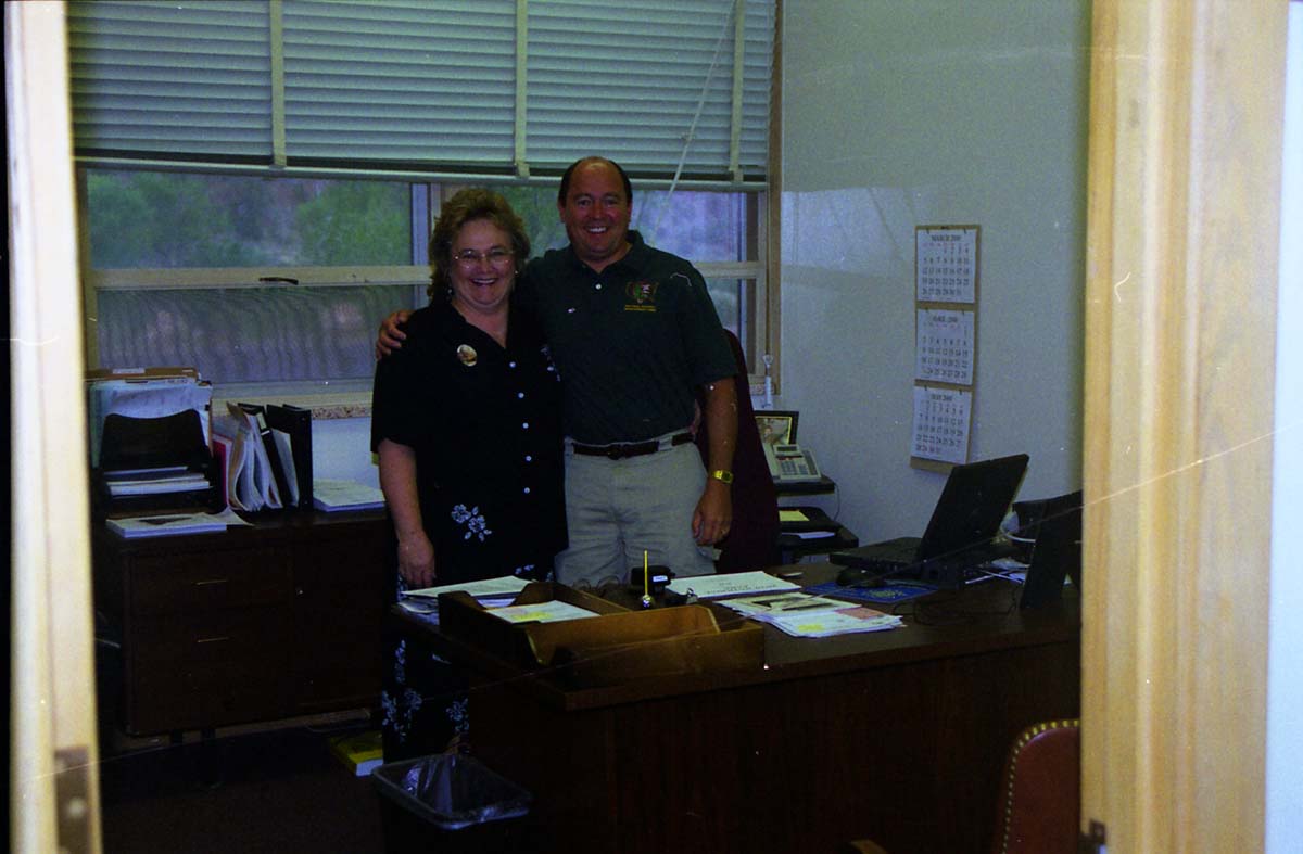 Color Photos of administration personnel. Man and woman standing by desk.