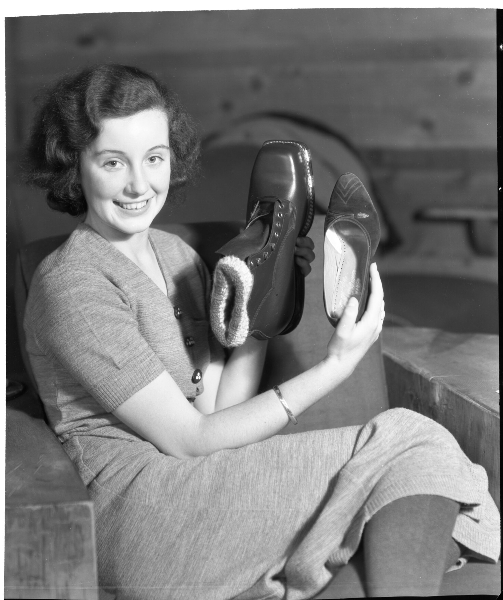 Miss Peggy Gamble - "Miss Australia" at Badger Pass. Miss Gamble considers ski shoes and compares them with her slippers on recent visit to Badger Pass Ski House just completed this season.