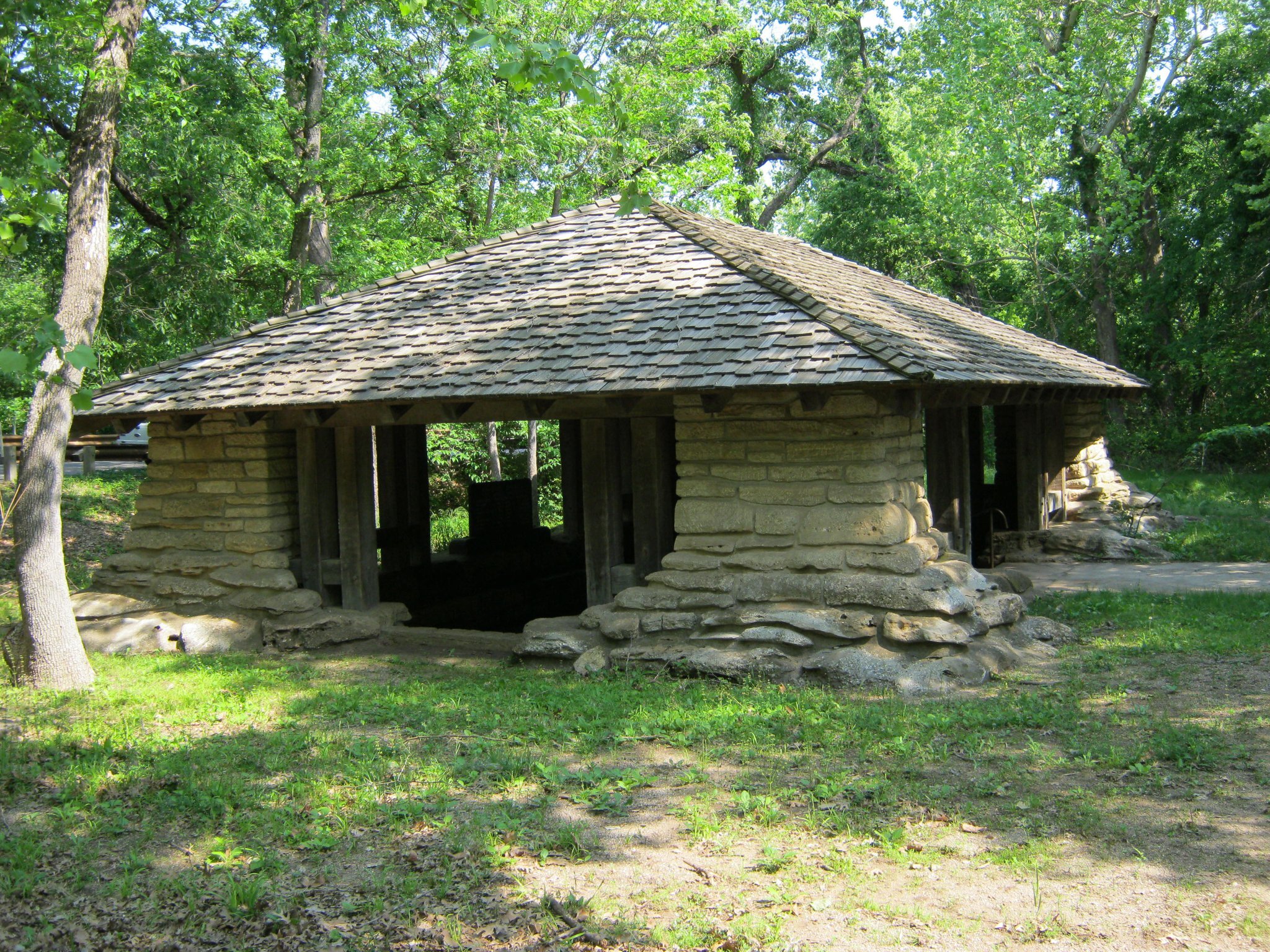 Stone pavilion with shingled roof; wide stone pillars that swell at the base.