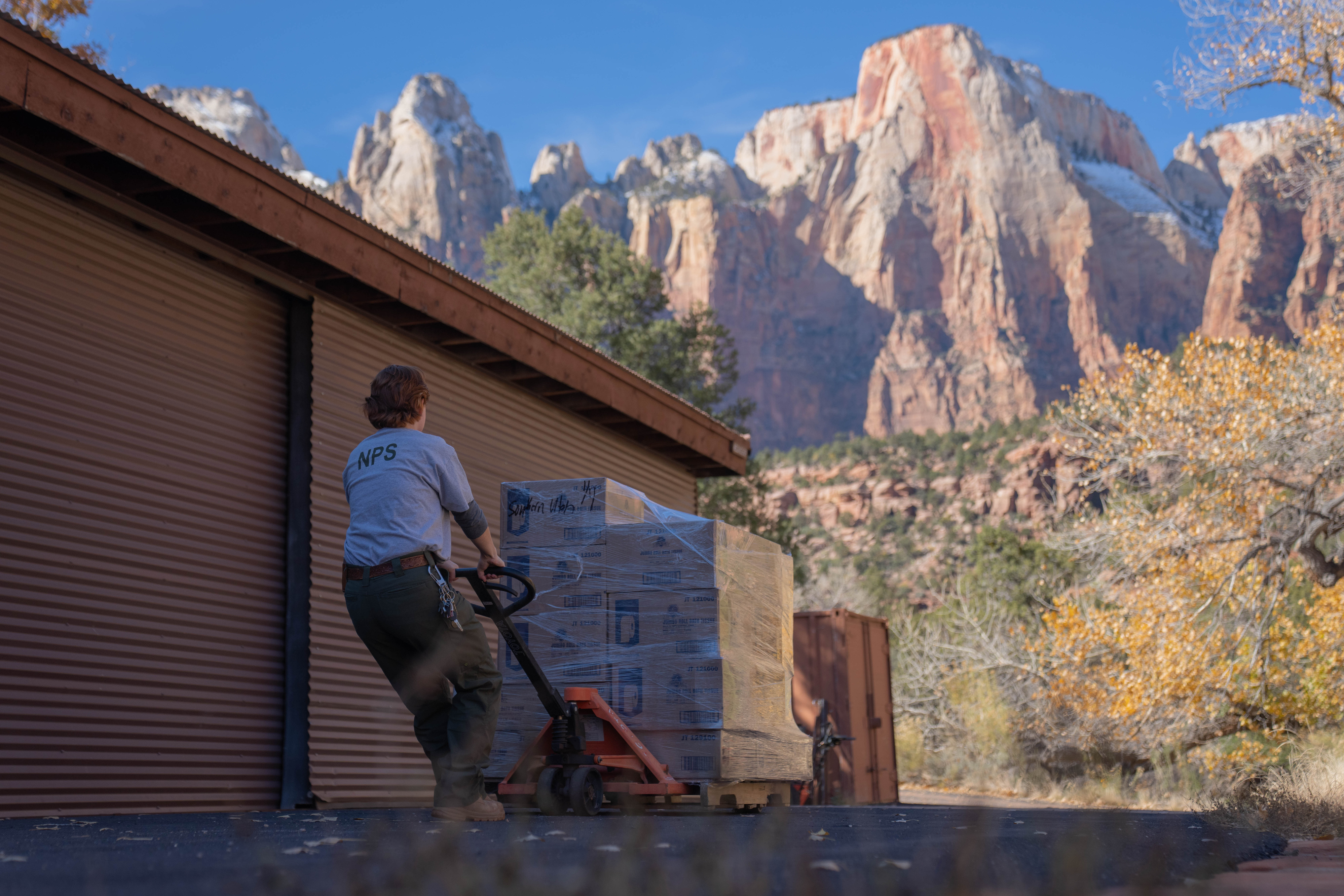 A maintenance crew member pulls packages with sandstone cliffs in the background.
