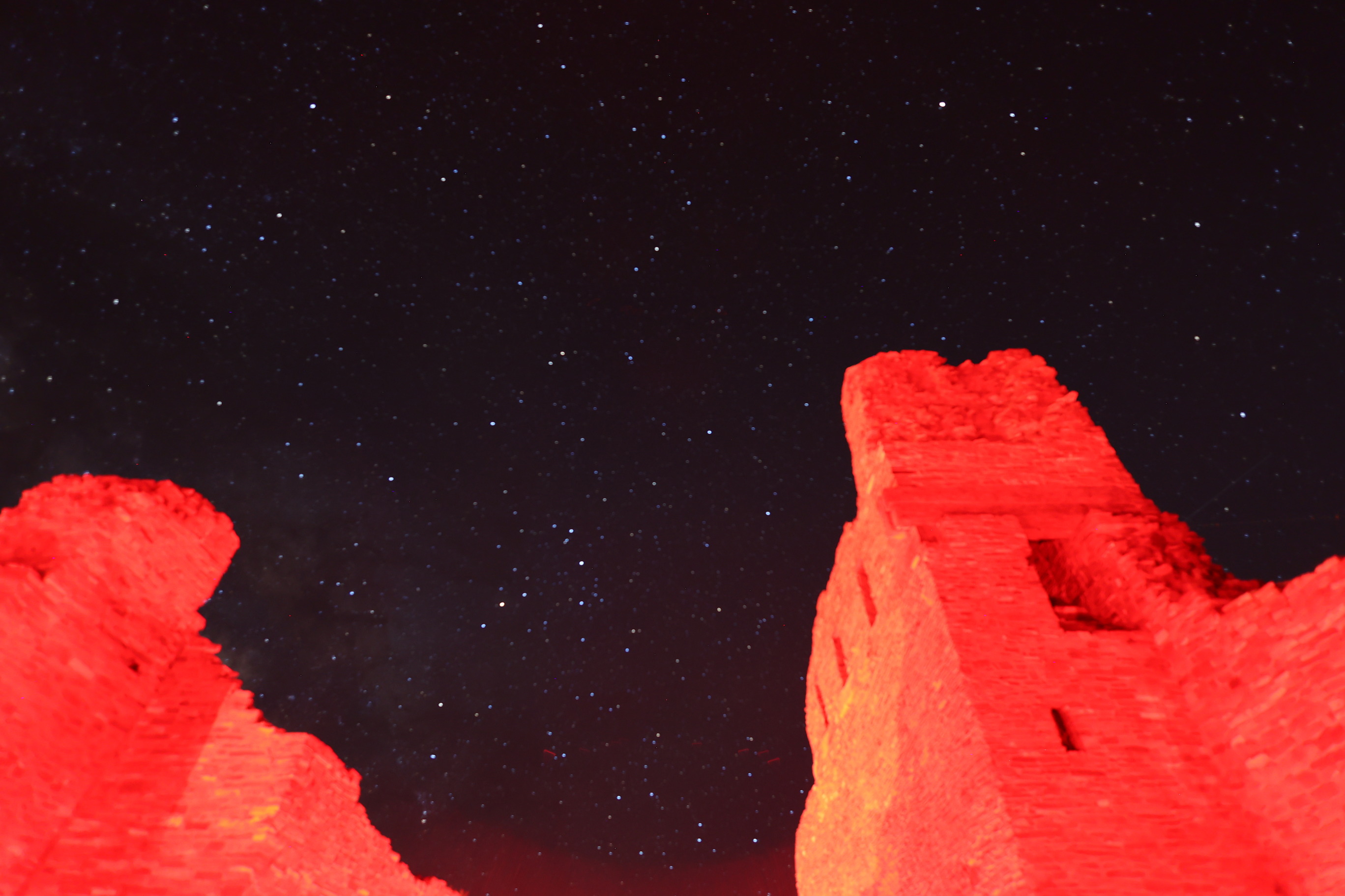 Dark sky image with a small cluster of bright stars and church remnants in the foreground.