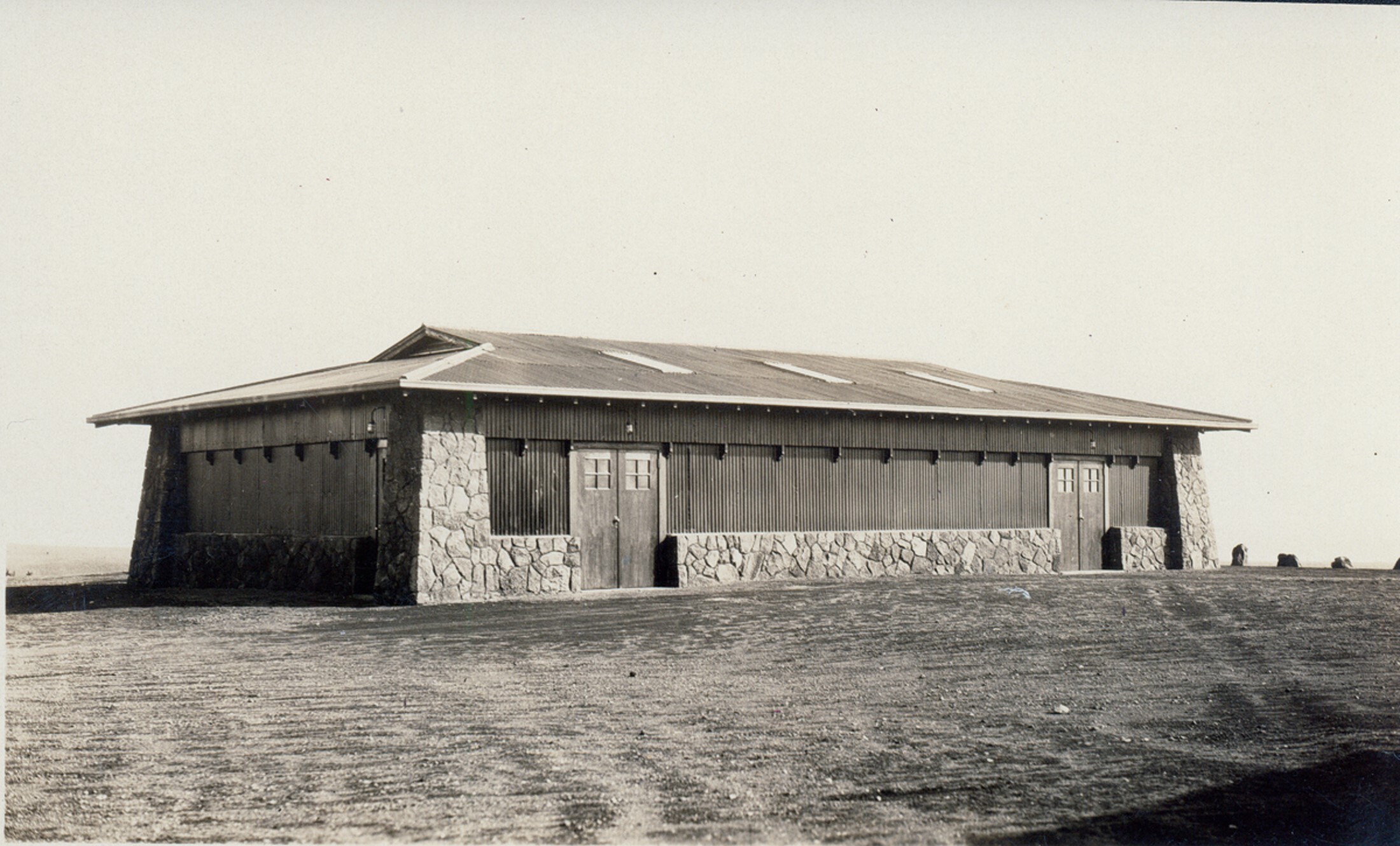 A black and white photograph of a building made with rock foundation and paneled with wood. 
