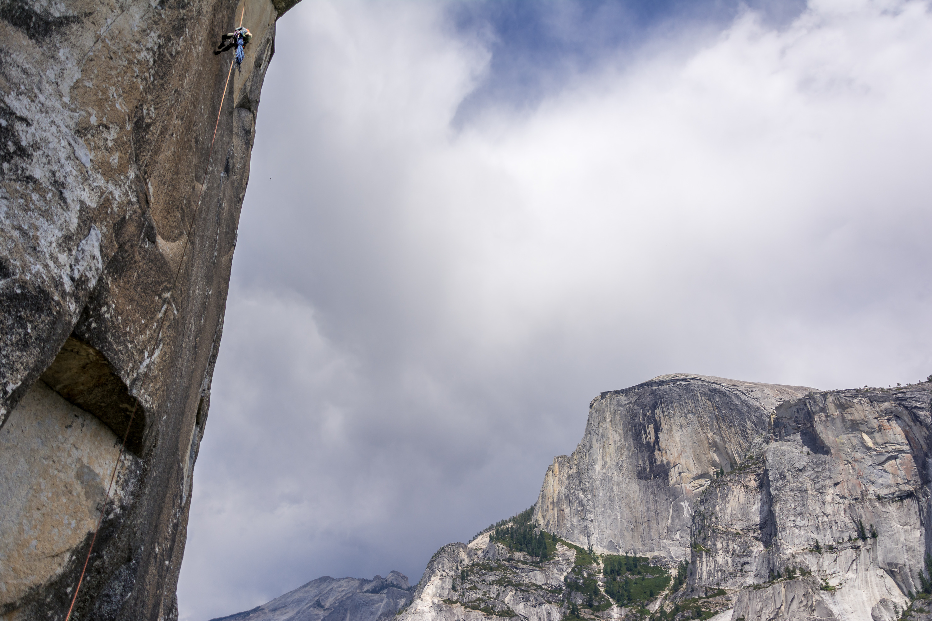 A climber rappels down a wall with Half Dome in the background. 