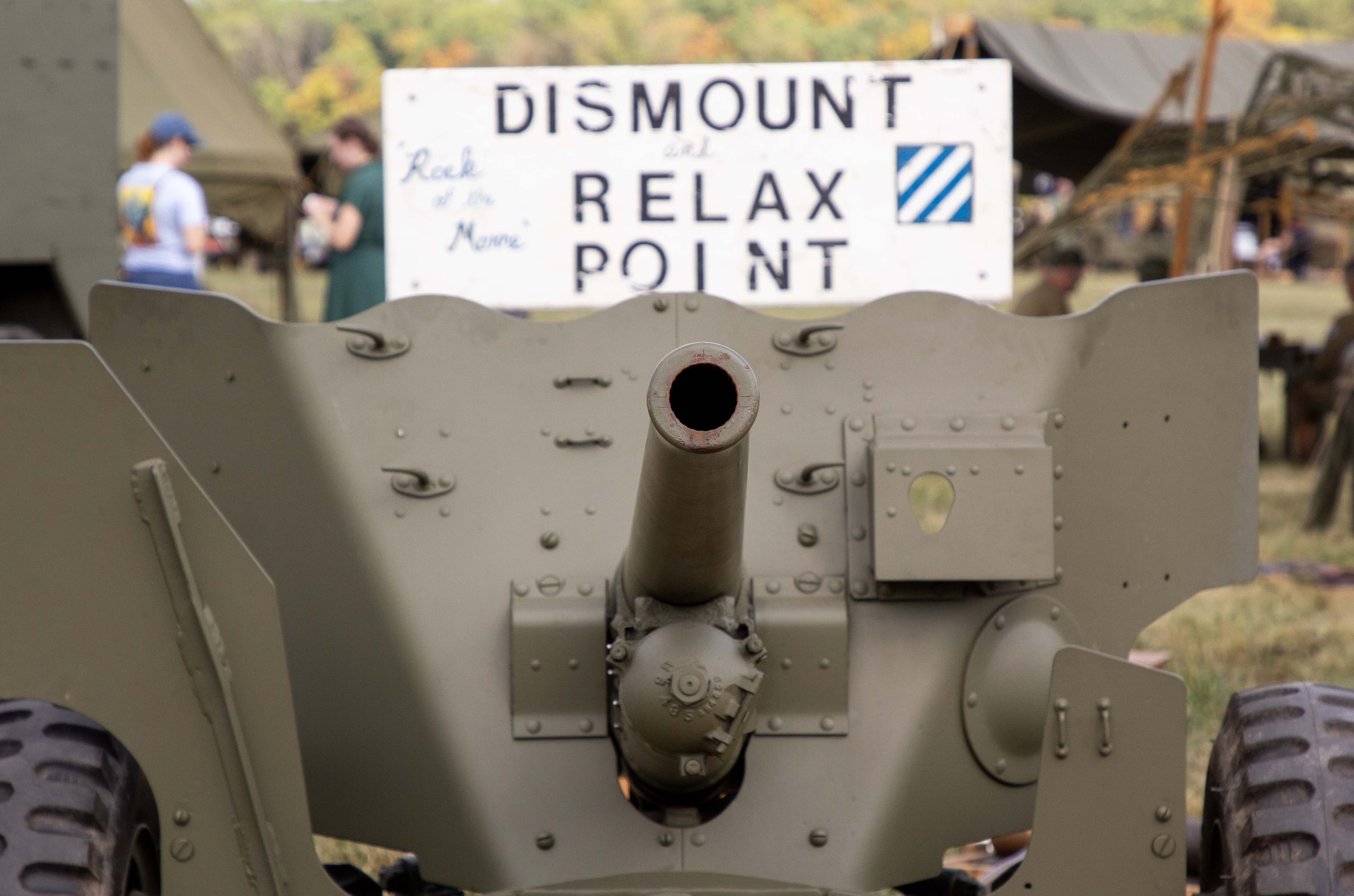 A green historic vehicle with a long gun barrel. A sign behind says “Dismount and Relax Point” 
