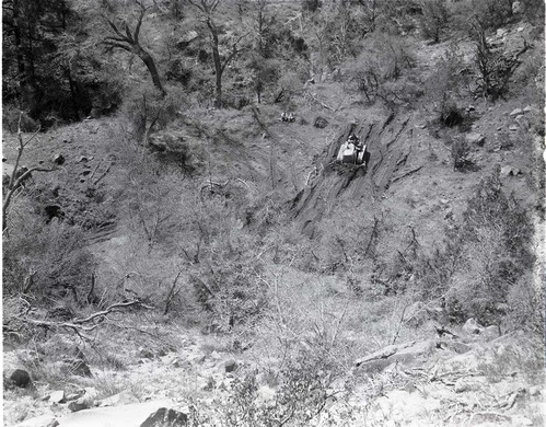 Bulldozer widening catchment area at top of pipeline - Springdale water system. Two men seated on hillside watching.