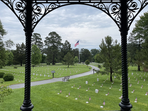 Decorative wrought iron frames a landscape view of American Flags in front of white marble headstones.
